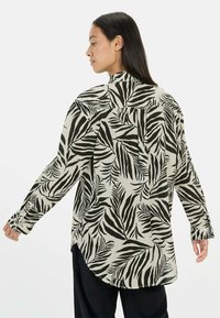 Langarmshirt van lichtgewicht stof met een zwart en crèmekleurig bladerenpatroon. Gebogen zoom en met knopen afsluitbare manchetten aan de mouwen.