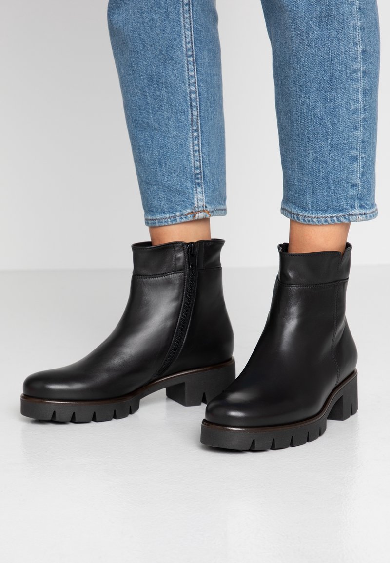 Bottines en cuir noir avec un design effilé, fermeture éclair sur le côté et une semelle épaisse à rainures. Associées à un denim retroussé.