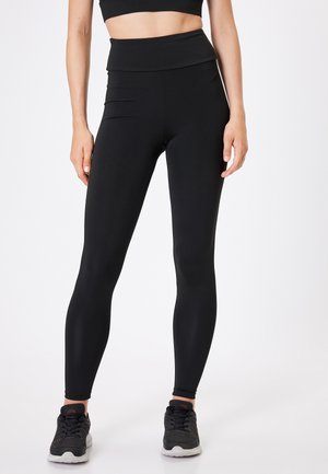 Leggings negros de cintura alta con una textura suave y elastizada. Detalles de costura sutiles en la cintura y los tobillos. Combinados con zapatillas deportivas negras.