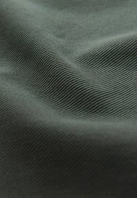 Tela textil en verde oscuro con una sutil textura acanalada, que muestra curvas suaves y suaves olas, destacando su naturaleza blanda y flexible.