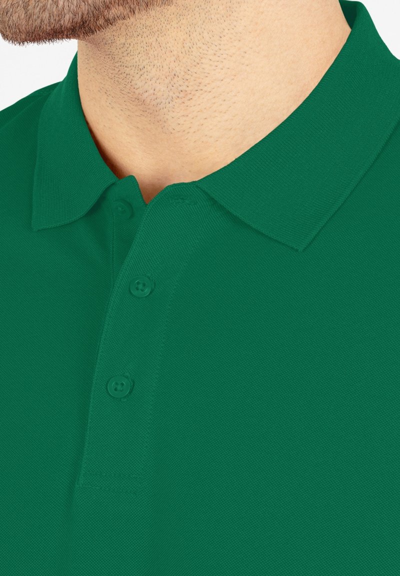 Groene polo met een gestructureerde stof, voorzien van een kraag en een drie-knopen sluiting. Close-up toont het halsgebied en de details van het shirt.