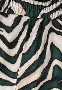 Gros plan sur un tissu de taille élastique présentant un motif rayé zèbre vert et beige avec une texture lisse et un léger aspect brillant.