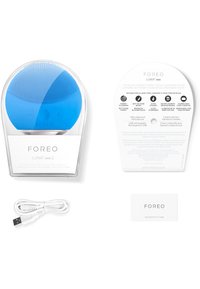 Blå silikon ansiktsrenseanordning med teksturert overflate, USB-kabel, autentisitetskort og emballasje med bruksanvisninger.