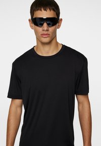 Svart kortärmad T-shirt med rund hals, tillverkad av ett mjukt, lätt material. Bärs med överdimensionerade svarta solglasögon.