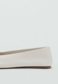 Zapato plano beige de piel lisa, con punta redondeada y un diseño de perfil bajo sin hardware ni adornos visibles.