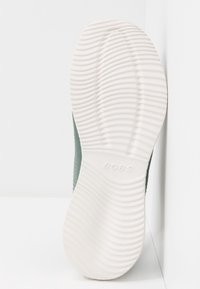 Semelle en caoutchouc blanche d'une chaussure avec des rainures horizontales texturées et le nom de marque "BOBS" embossé au centre.