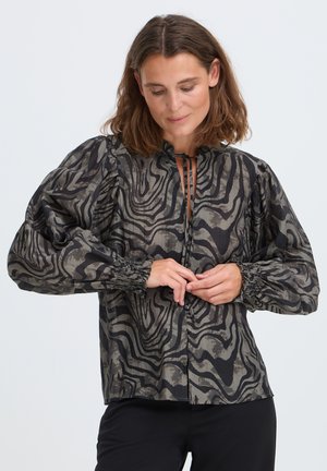 Woman fastening buttons on a long-sleeve black and gray patterned blouse with puffed sleeves and ruffled collar.