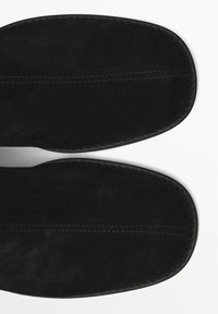Chaussons en suède noir avec un bout arrondi, texture lisse, coutures contrastées le long du bord et semelle intérieure rembourrée.