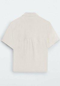 Kurzärmliges, hellbeiges Hemd mit umklappbarem Kragen und Raffung im Rücken, aus einem weichen, atmungsaktiven Stoff gefertigt.