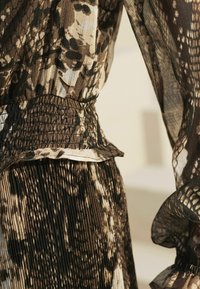 Robe froncée dans des teintes de marron et de beige, avec un motif texturé et des accents volantés au bas et aux bords des manches.