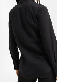 Svart långärmad skjorta med en mjuk textur, som har en klassisk krage, knäppta manschetter och en böjd fåll.