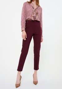 Bordeauxbroeken gecombineerd met een blouse met een patroon en een strik halslijn. Soepele stof, tapered leg ontwerp en bruine hakken.