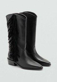 Cizme de cowboy din piele neagră cu vârf ascuțit, având ciucuri negri verticale pe partea exterioară și modele în relief cu frunze pe tija cizmei.