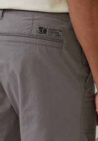 Shorts gris décontractés en tissu texturé, dotés d'une poche arrière avec un logo en patch noir portant l'inscription "s.O.C. Elevated Casual Est. 1969."