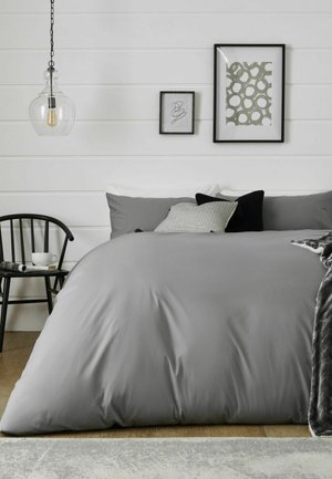 Bett mit grauer Bettwäsche und dekorativen Kissen, schwarzer Stuhl mit Tasse und Magazin, zwei gerahmte abstrakte Kunstwerke und hängende Glas-Pendelleuchte.