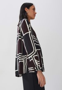 Black and white long-sleeve shirt with geometric pattern; lightweight fabric; buttoned cuffs; loose fit with a straight hem.
