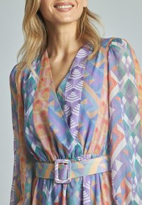 Mehrfarbiges Kleid mit geometrischen Mustern in Pastelltönen. Leichter Stoff, taillierter Schnitt und lange Ärmel mit puffigen Schultern.