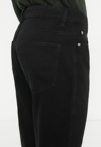 Jeans in denim nero con una silhouette slim, dotati di due tasche posteriori e con dettagli in metallo argentato vicino alla vita. Tessuto testurizzato.