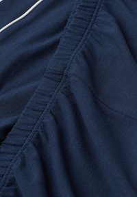 Marineblauwe stof met een soepele textuur, voorzien van elastische rimpeling langs de naad en een contrasterende witte accentsteek.