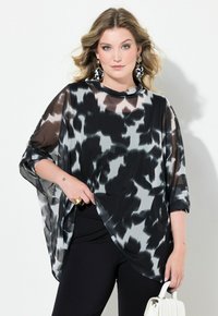 Top trasparente in bianco e nero con un motivo astratto, dalla vestibilità ampia, maniche corte e scollatura rotonda, abbinato a pantaloni neri.