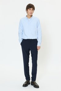 Šviesiai mėlyna marškiniai su sagomis, tamsiai mėlynos kelnės ir blizgančios juodos batai. Marškiniai turi klasikinį apykaklę, o kelnės yra pritaikytos.