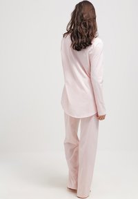 Conjunto de ropa de casa de color rosa claro que incluye una camiseta de manga larga con dobladillo curvado y pantalones de pierna ancha a juego, fabricado en una tela suave y lisa.