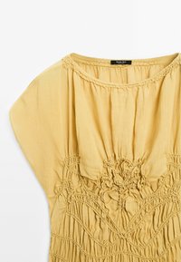 Geel katoenen jurk met een losse pasvorm, voorzien van gegulde smockdetails, een ronde halslijn en brede korte mouwen.