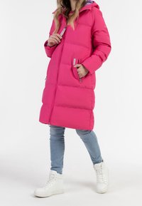 Rosa Daunenjacke mit Kapuze, gestepptem Design, zwei Reißverschluss-Taschen und einem Frontreißverschluss. Kombiniert mit hellblauen Jeans und weißen Sneakers.