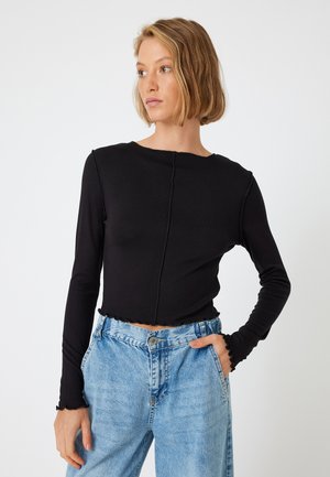 Zwarte lange mouw top met een ronde hals, rafelige randen en een cropped pasvorm, gecombineerd met lichtblauwe high-waisted jeans.