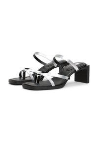Sandalias de tacón negro con correas plateadas, diseño de punta abierta, tacón cuadrado, textura suave y detalles de correas entrelazadas.