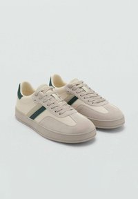 Zapatillas beige hechas de ante y algodón, con acentos verdes y un diseño de puntera redonda, suela de goma plana y cierre con cordones.