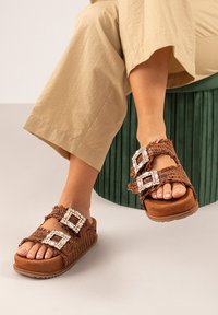 Sandalias trenzadas marrones con dos grandes hebillas decorativas. Presentan una suela gruesa y acolchada y un upper texturizado.