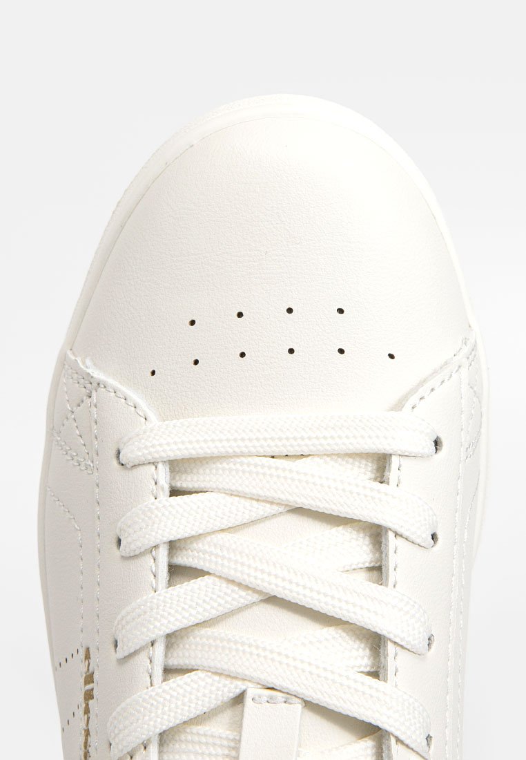 Baskets en cuir blanc avec un bout arrondi, une surface texturée et des lacets plats. Présente des trous de ventilation sur la languette et un design latéral subtil.