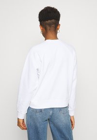 Vit sweatshirt med avslappnad passform, raglanärmar, ribbade muddar och nederkant. Buren med ljusblå denimjeans. Slät textur.