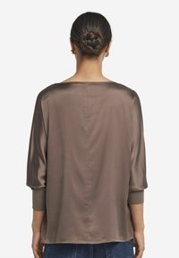 Blusa di raso marrone con maniche a tre quarti, vestibilità comoda e scollatura ampia. Texture liscia e design semplice con colore uniforme.