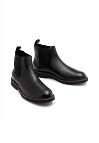 Czarne skórzane botki za kostkę z elastycznymi panelami bocznymi, okrągłymi czubkami i uchwytami do zakładania. Posiadają brązową podeszwę dla kontrastu oraz teksturowaną cholewkę.