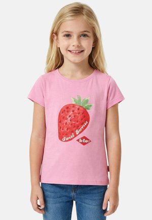 Jeune fille souriante, portant un t-shirt rose avec une grande fraise rouge et le texte « Sweet Berries », assorti à un jean bleu.