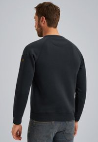 Donkergrijze sweatshirt met raglanmouwen, ribgebreide boorden en zoom, en een patchdetail op de linker mouw. Zachte, textuurstof.
