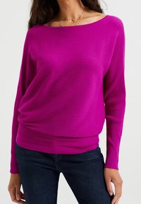 Fuchsia långärmad tröja med ribbat mönster och vid halsringning, med en figurnära midja och avslappnad passform, i kombination med mörk denim.