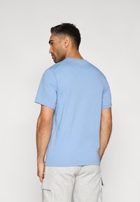 Ανοιχτό μπλε κοντομάνικο μπλουζάκι από βαμβάκι. Στυλ με στρογγυλή λαιμόκοψη και ομαλή υφή. Φορεμένο με γκρι φόρμες, παρουσιάζοντας casual εφαρμογή.