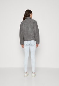 Veste en simili cuir gris avec une finition légèrement texturée, dotée d'un large col et d'une coupe décontractée, associée à un jean skinny bleu clair et des baskets.