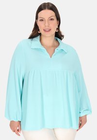 Hellblaue gestreifte Bluse mit Kragen, langen Ärmeln und geraffter Taille. Hergestellt aus einem weichen, strukturierten Stoff.