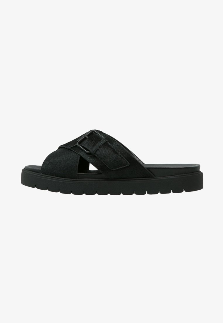 Sandale noire slip-on avec semelle épaisse et larges brides croisées avec une boucle réglable sur le dessus.