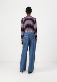 Langermet, stripete t-skjorte i marineblå, rød og hvite farger, parret med høy midje, vide blå jeans med baklommer.
