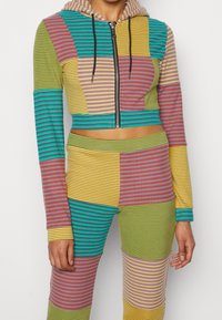 Survêtement deux pièces composé d'un sweat à capuche court zippé avec un motif rayé multicolore en vert, bleu, jaune, rose et violet.