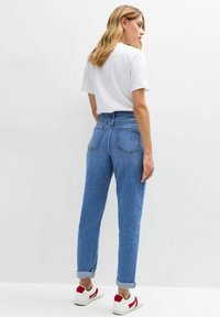 Blauwe denim jeans met hoge taille, een losse pasvorm, opgerolde pijpen en achterzakken, gecombineerd met een wit T-shirt en casual sneakers.