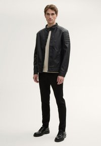 Giubbotto in ecopelle nera con colletto alto, dettagli trapuntati sulle spalle e chiusura con zip. Abbinato a pantaloni e scarpe neri.