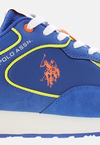 Modré tenisky s vrchnou časťou z semišu a syntetického materiálu, limetkovo zelené akcenty, biele šnúrky a oranžové logo jazdca na boku.