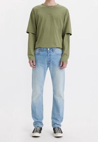 Camiseta de algodón verde claro combinada con pantalones vaqueros de mezclilla azul claro. Zapatillas completan el look. La camiseta tiene mangas oversize y un ajuste casual.