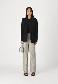 Zwarte blazer, nauwsluitend zwart topje, glanzende zilveren wijde broek met een gestructureerd patroon, zwarte sandalen en een kleine grijze handtas.